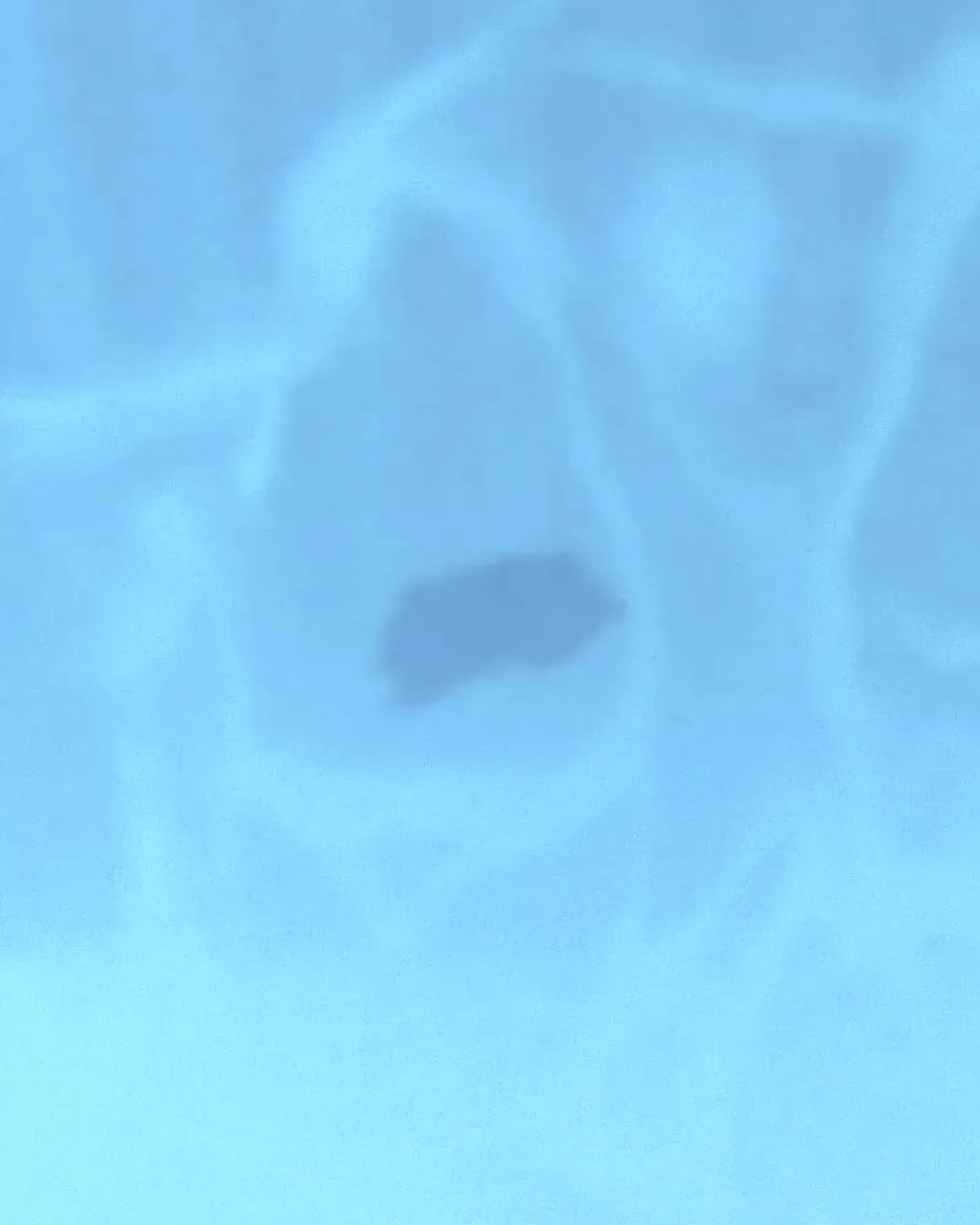 Clear blue pool water with light ripples over a sandy bottom near the shallow end.
