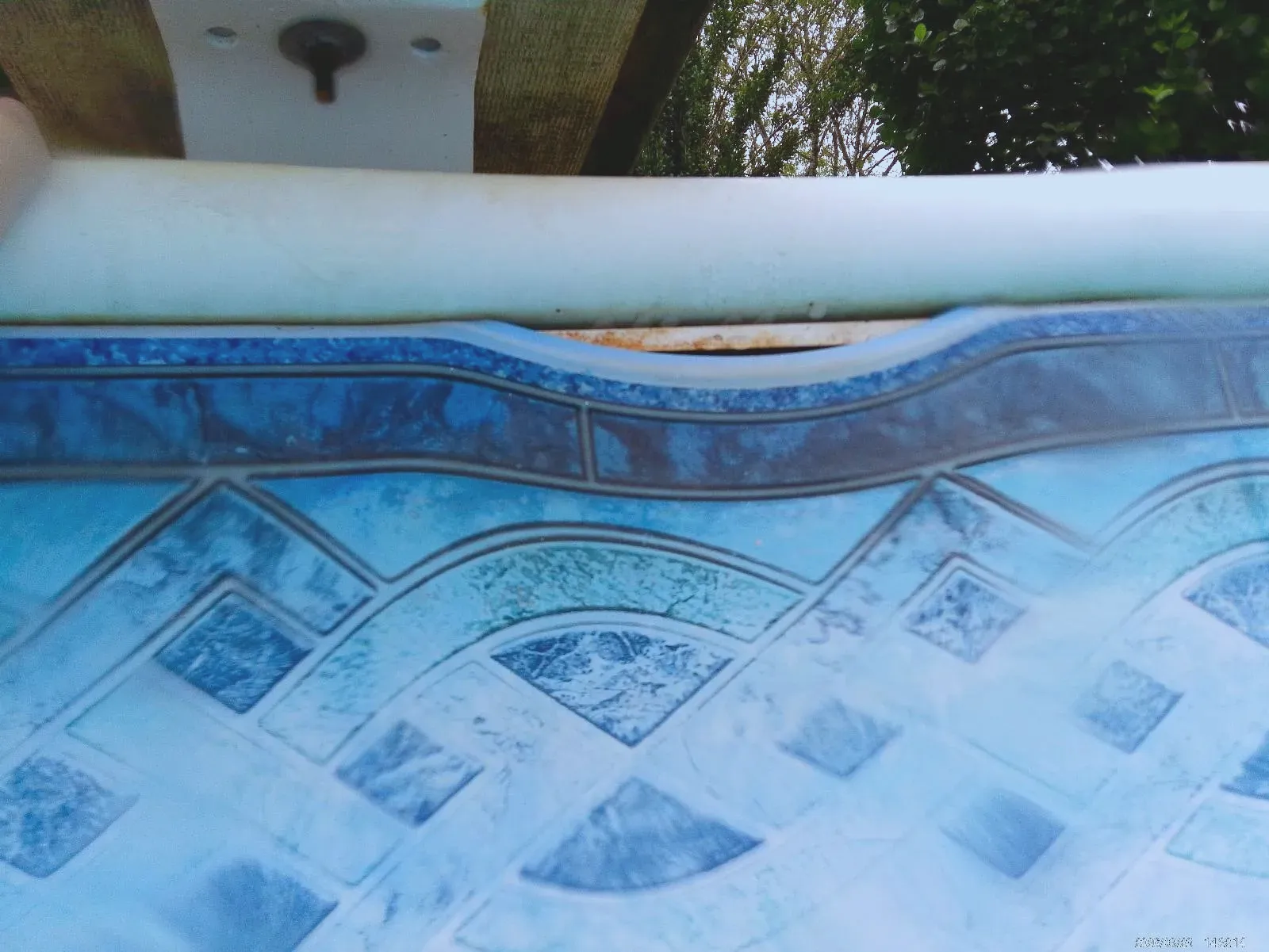 Pool liner bead pulling away from the top rail, exposing the wall beneath the patterned lining.